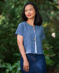 a woman standing in front of trees wearing a blue shirt and denim skirt with buttons