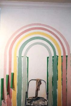 a cat sitting on top of a chair in front of a rainbow painted wall