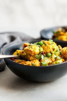 two black bowls filled with food sitting on top of a white tablecloth next to a gray towel