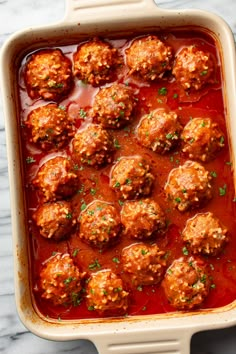 meatballs covered in marinara sauce in a casserole dish on a marble surface