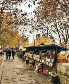 people walking down the sidewalk in front of a book stand with lots of books on it