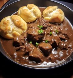 a black plate topped with meat and biscuits covered in gravy on top of a wooden table