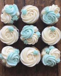 twelve cupcakes with blue frosting sitting on top of a wooden table