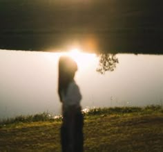 a person standing in front of a body of water with the sun setting behind them