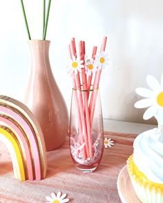 there are pink and yellow straws in the vase with daisies on the table