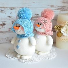 two snowmen are sitting on a doily next to a candle and some flowers