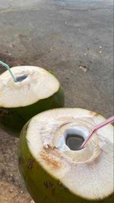 two coconuts with straw in them sitting on the ground