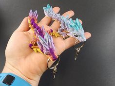 a hand holding two dragon keychains in it's left hand, with another one on the other side