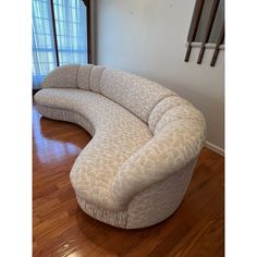 a curved couch sitting on top of a hard wood floor next to an open window