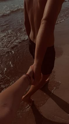 a man holding the hand of a woman on the beach with waves crashing in behind him