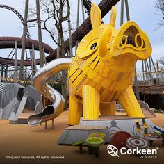 a large yellow elephant statue sitting in the middle of a park with other rides and roller coasters