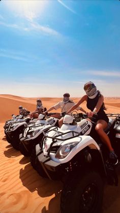 four people riding on four wheelers in the desert with sand dunes and blue sky