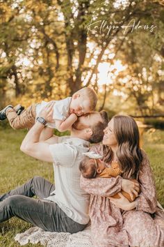 a man holding a baby while sitting on top of a woman's lap in the grass