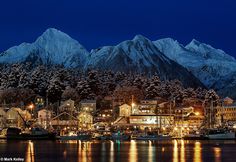 the mountains are covered in snow and lit up by lights at night, with boats docked on the water