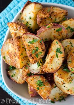 a white bowl filled with potatoes covered in seasoning and garnished with parsley