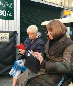 two women sitting on a bench in front of a building