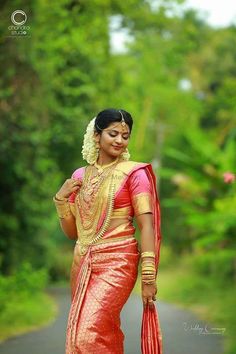 a woman in a red and gold sari is walking down the road with her hand on her hip