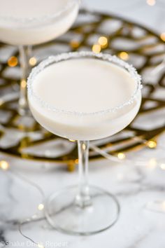 two martinis sitting next to each other on a marble counter top with christmas lights in the background