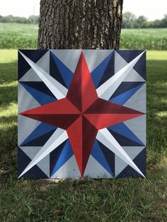 a red, white and blue star quilt hanging from a tree in front of a field