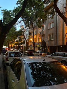 cars are parked on the street in front of tall buildings and trees with lights at night