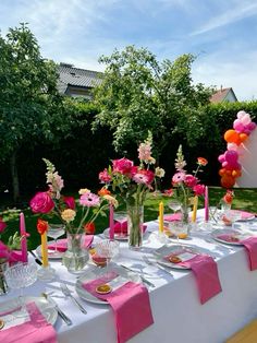 the table is set with pink and orange flowers, candles, plates and napkins