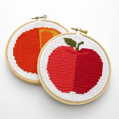 two cross stitch hoops with an apple and orange on them, one is red