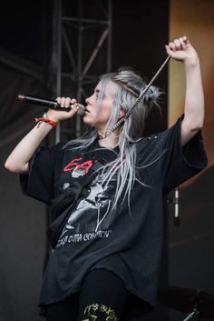 a woman with white hair and piercings on her head is singing into a microphone