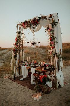 a wooden table topped with flowers and candles on top of a sandy beach near the ocean