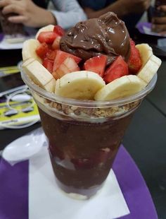 a dessert in a plastic cup with chocolate sauce and strawberries on the side,