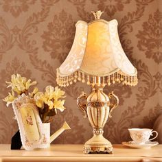 a table with a lamp, teapot and flowers on it next to a wall paper