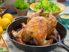 a close up of a chicken in a pan on a table with lemons and lettuce