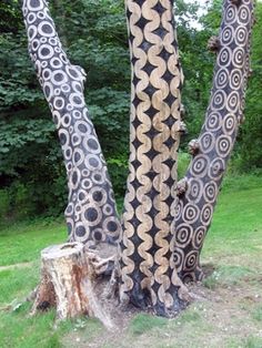 the trunk of a tree with intricate designs on it's bark, in front of some green grass and trees