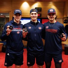 three men in blue jackets and hats holding up some dumbs while standing next to each other