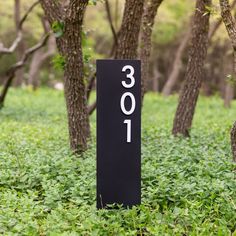 a black sign that is in the grass near some trees and bushes with numbers on it