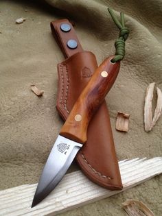 a knife and sheath laying next to each other on the sand with some wood shavings around it