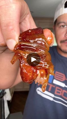 a man holding up a piece of bacon in front of his face while wearing a hat