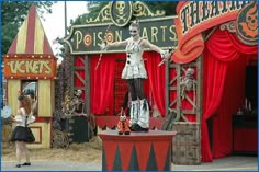 a woman standing on top of a stage in front of a circus booth with skeleton decorations