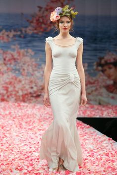 a woman walking down a runway wearing a dress with flowers on it's head