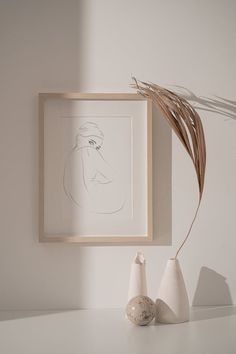 two white vases sitting on top of a table next to a framed art piece