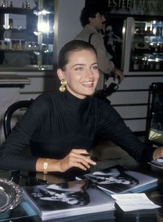 a woman sitting at a table smiling and posing for the camera in front of some photographs