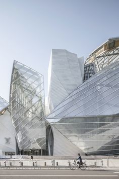 a man riding a bike past a building with large glass panels on it's sides