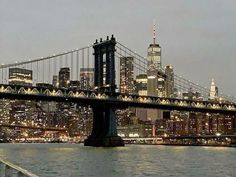 the city skyline is lit up at night as seen from across the water in new york