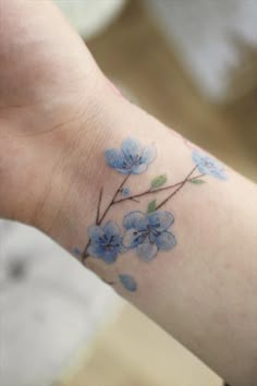 a small wrist tattoo with blue flowers on it