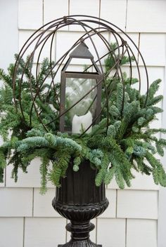 a candle is sitting on top of a vase with greenery in front of a house