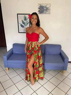 a woman standing in front of a blue couch wearing a red top and floral print skirt