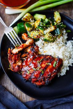 a black plate topped with chicken, rice and veggies