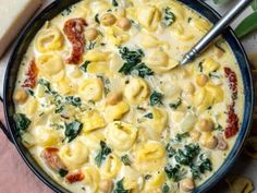 a bowl filled with pasta and spinach on top of a pink cloth next to bread