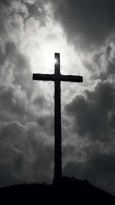 a cross on top of a hill with the sun shining through clouds in the background