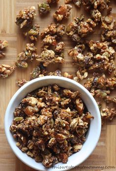 a white bowl filled with granola sitting on top of a wooden cutting board next to nuts