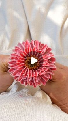 a person holding a pink flower in their left hand with a white shirt behind them